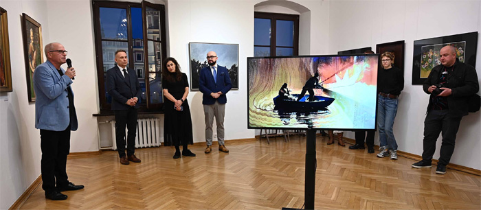 Na pierwszym planie widoczny monitor z wyświetloną animacją, w tle przemawiający dyrektor BWA, wiceprezydent oraz kordynatorka Programu Edukacyjnego Multimedia dla Ilustracji